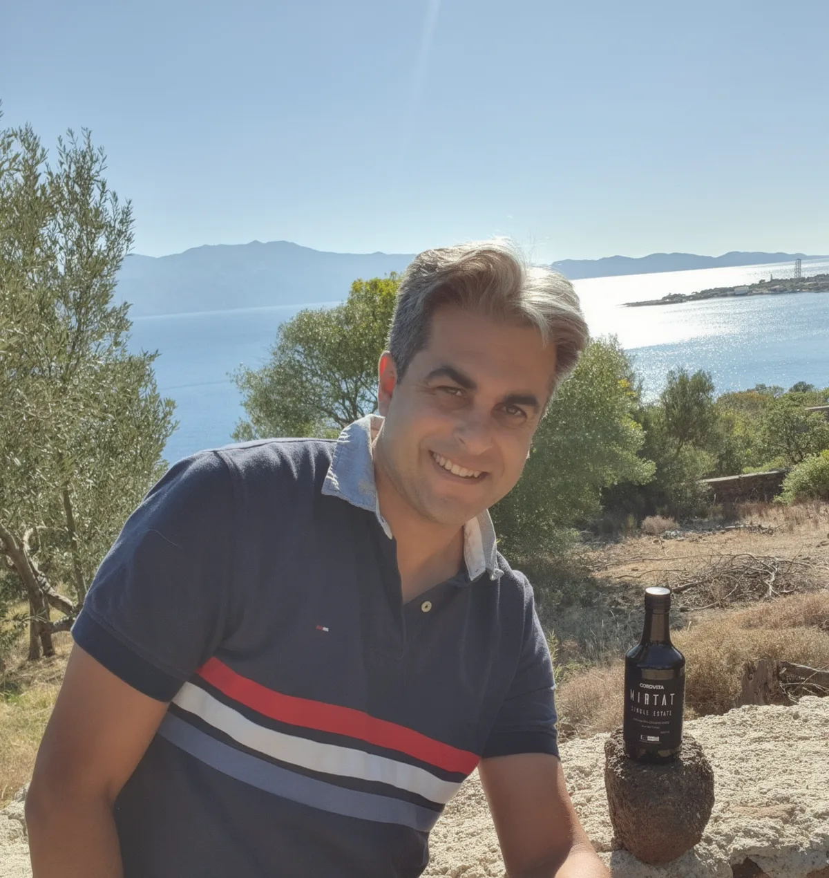 Deniz, Gründer von Corovita, mit einer Flasche Mirtat Single Estate vor der Ägäis